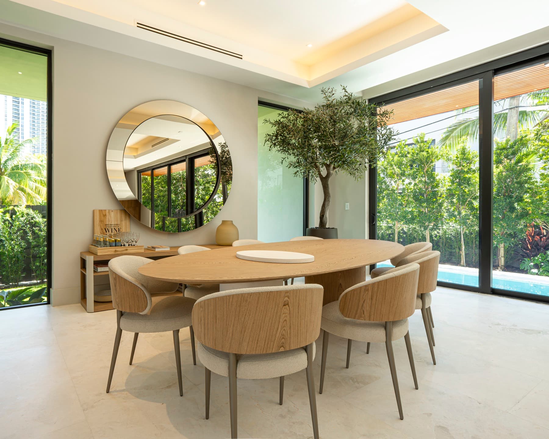 Sala de jantar com mesa oval de madeira aberta ao jardim da piscina